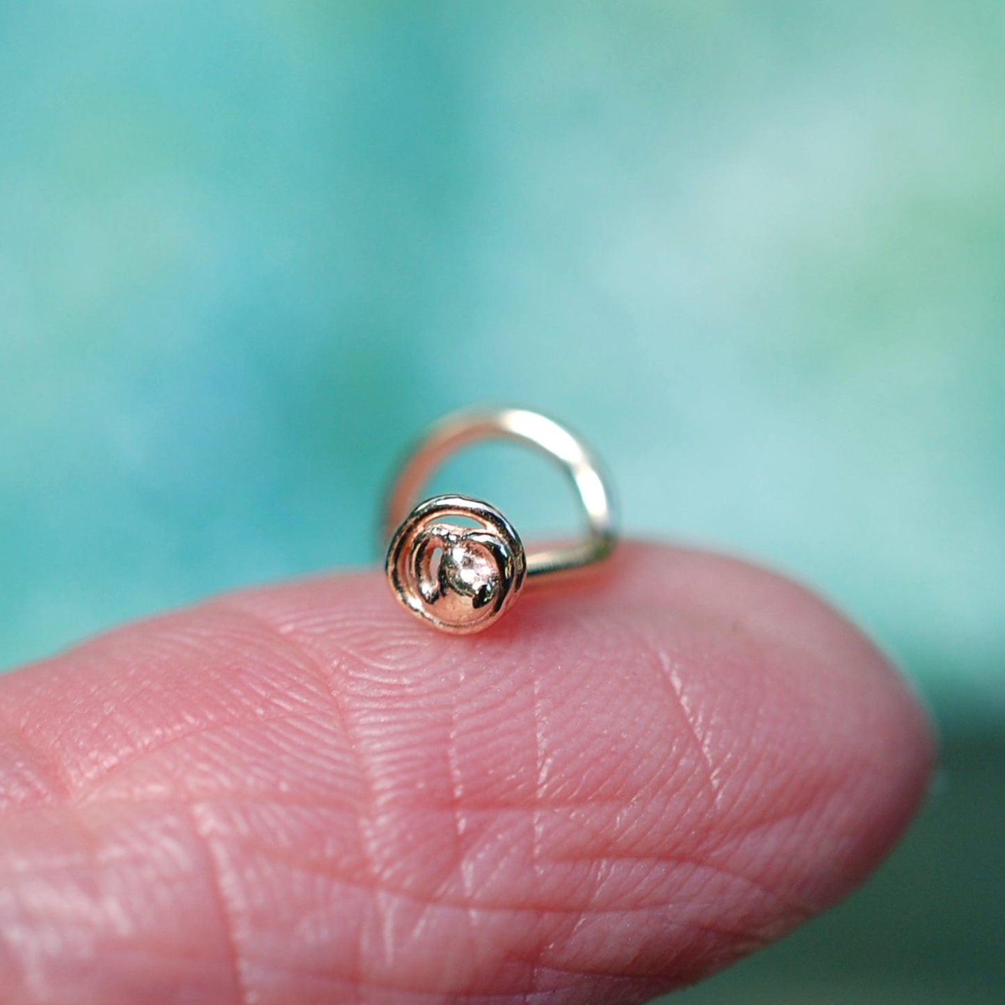 gold nose stud perched on a finger to show small size