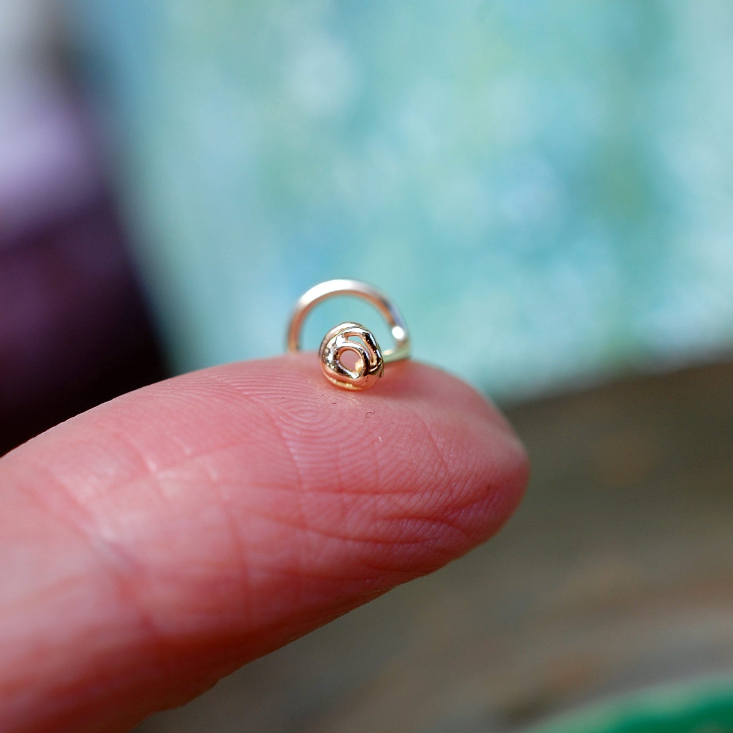 scribble nose stud in 14 karat gold perched on a finger to show tiny size