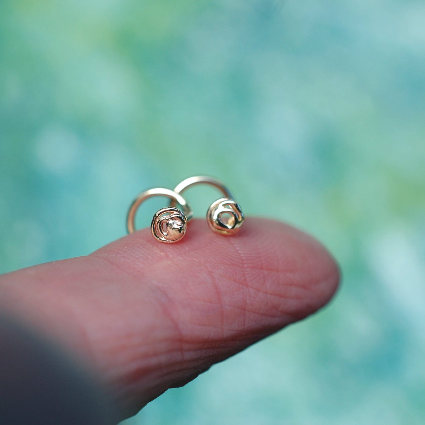 tiny gold nose studs on a finger shown for size. Scribble freeform pattern nose studs.
