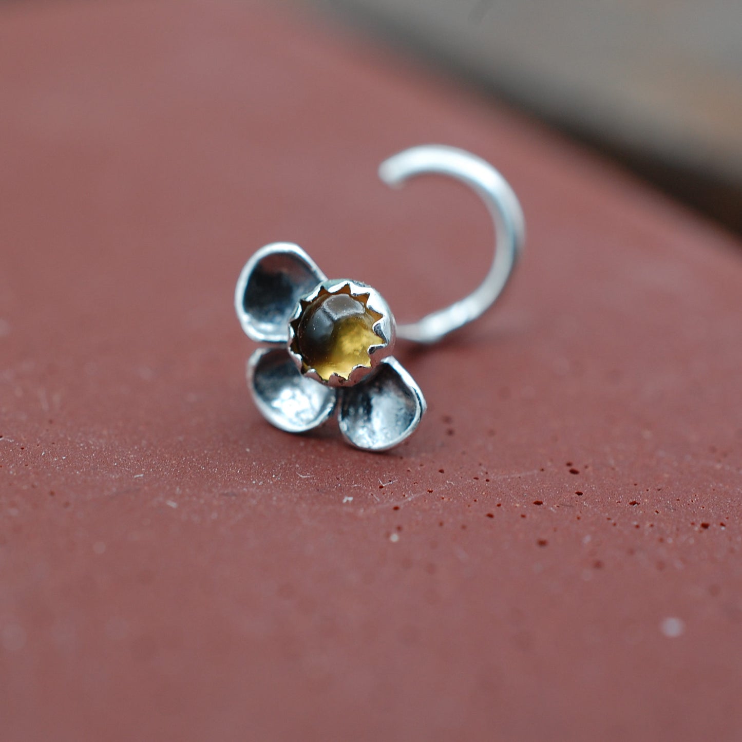 Silver flower-shaped nose stud on a red surface