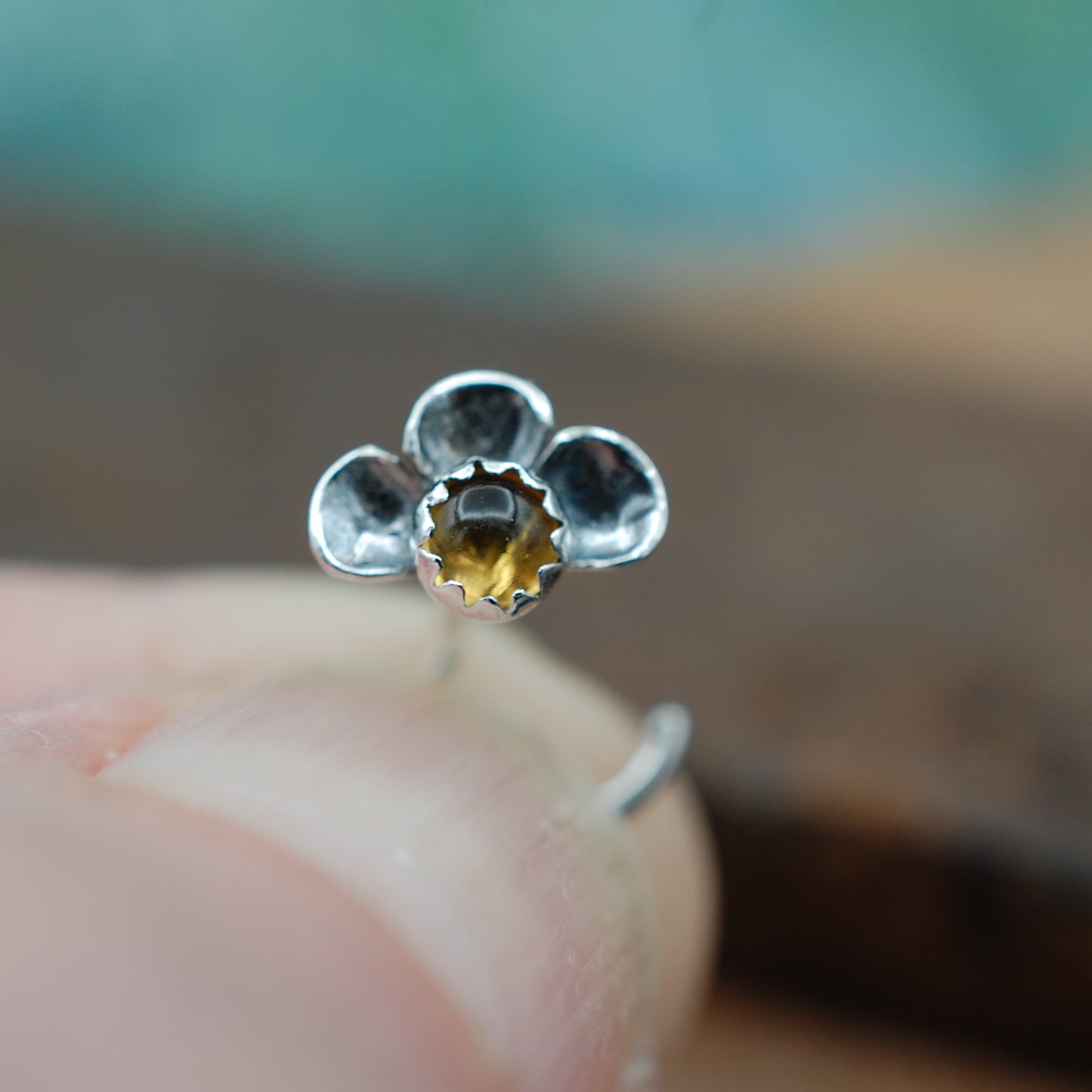 Silver flower-shaped nose stud held between fingers