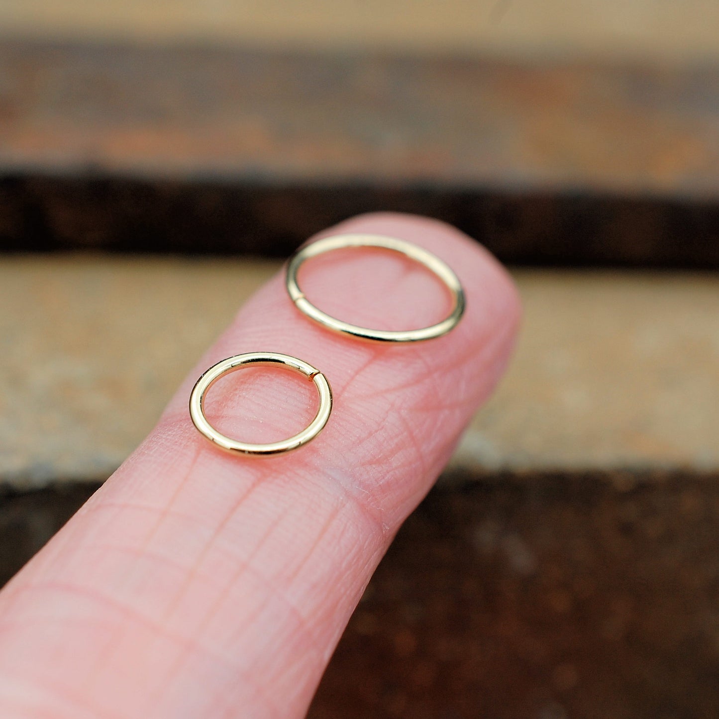 two gold nose rings on a finger for size comparison