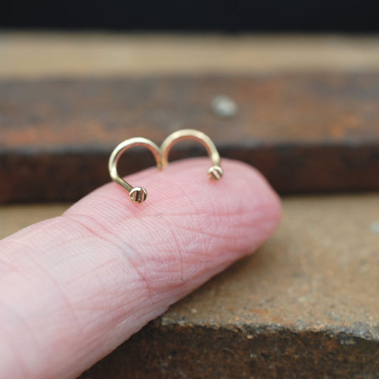 Gold nose stud on a finger against a rustic metal background