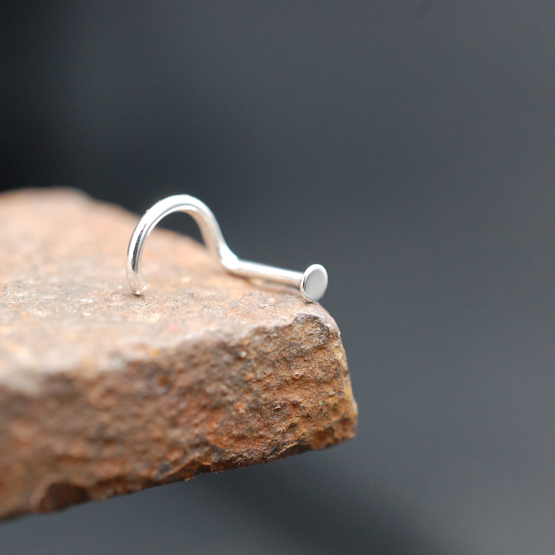 Silver nose stud on a textured stone surface with a dark background