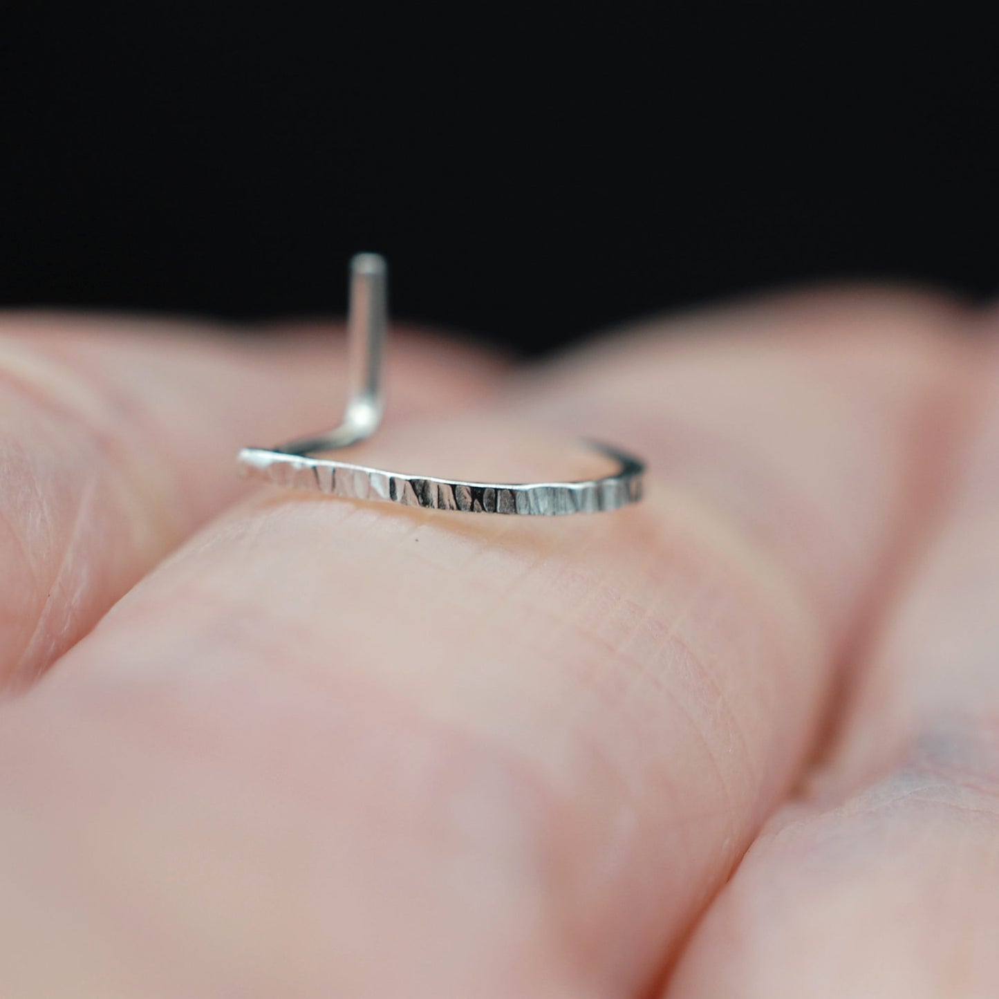 Silver nose ring on a person's finger with a blurred background