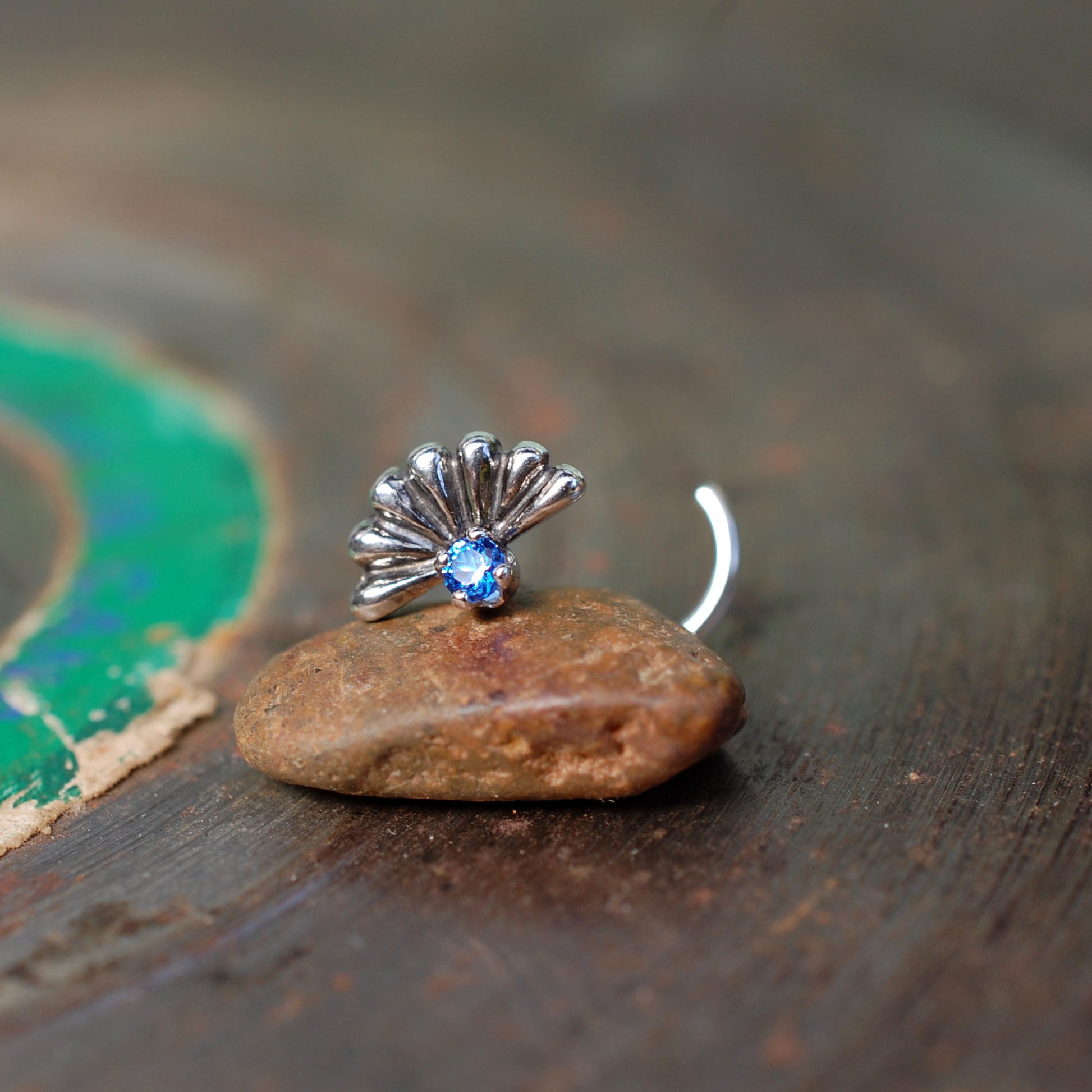sapphire nose stud with a big silver fan behind it