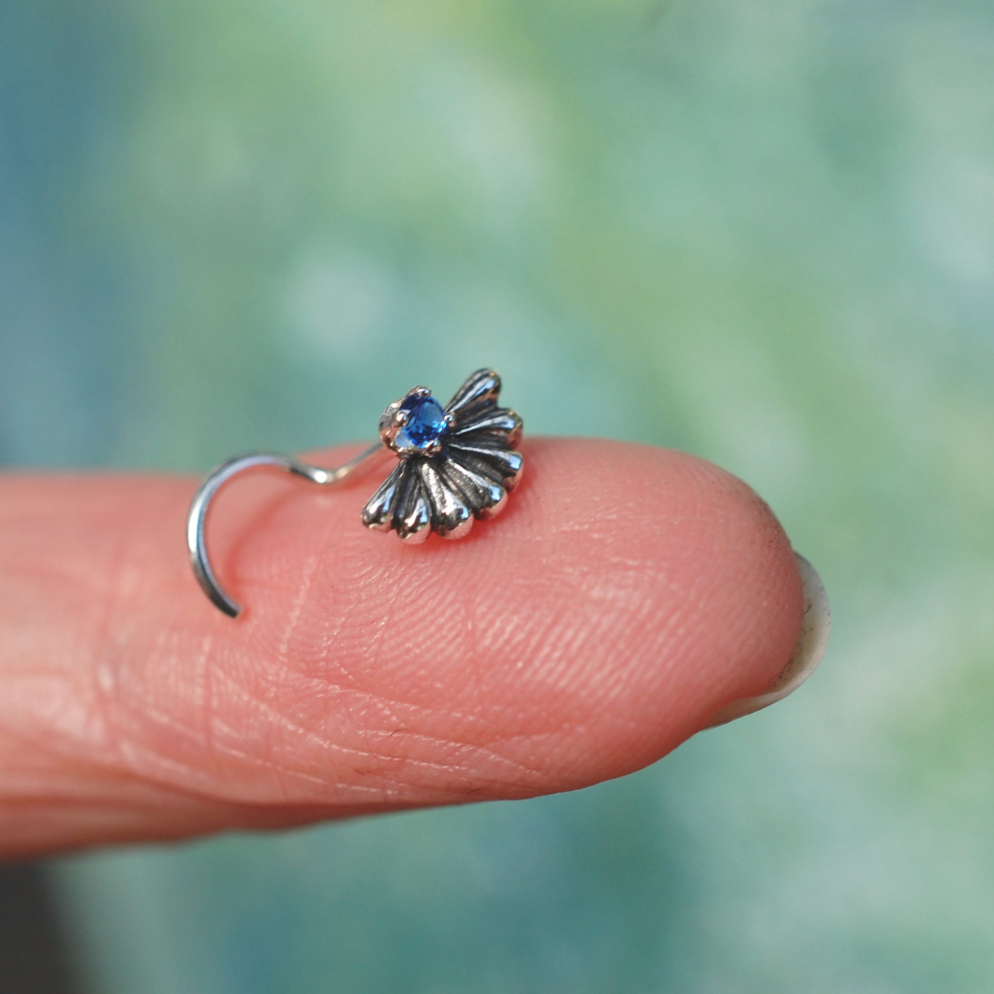 silver nose stud in a big fan shape with a sapphire gemstone
