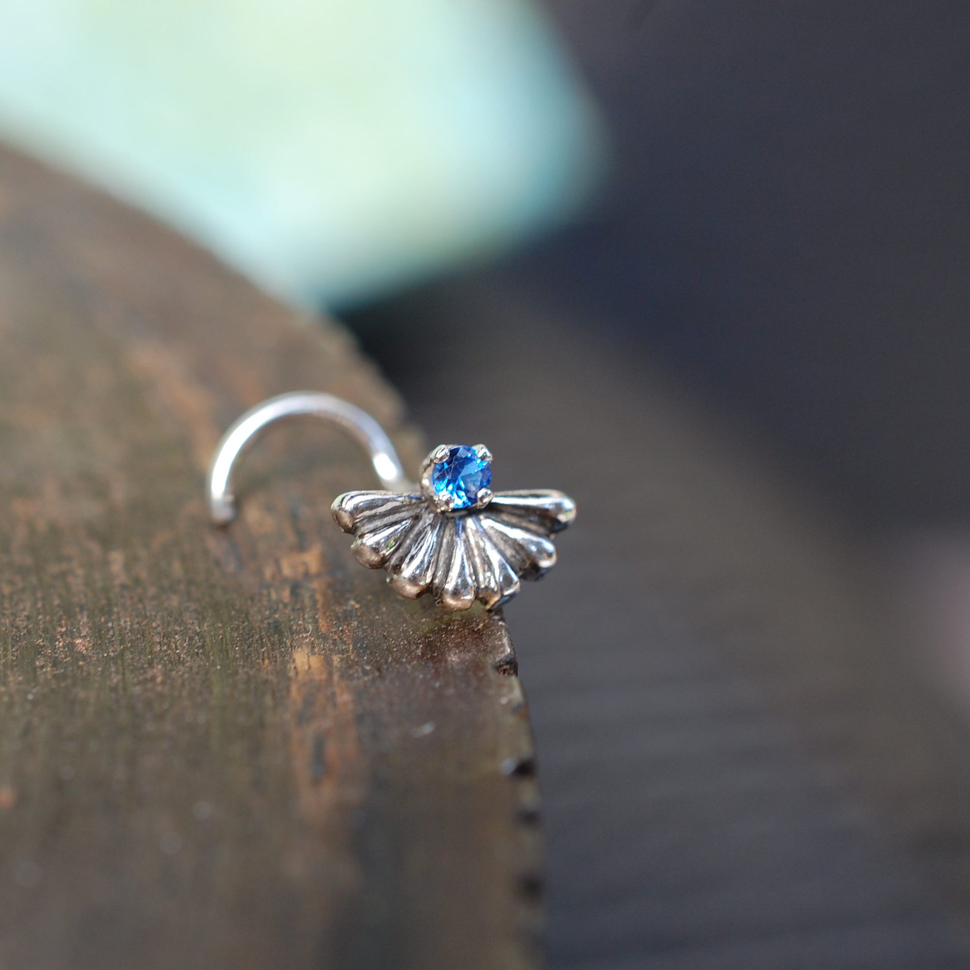big fan style nose stud in silver with a small blue gemstone
