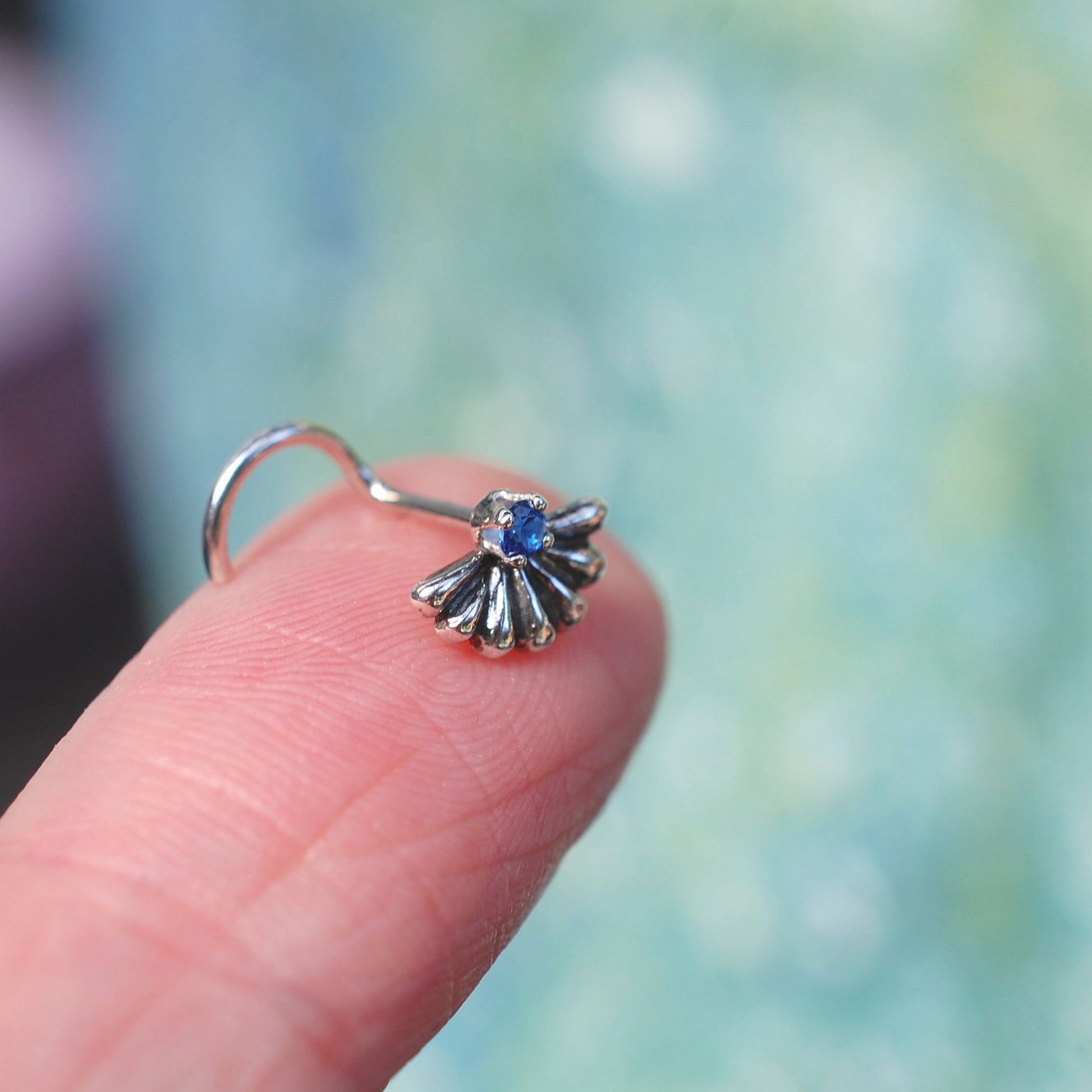 sapphire and silver nose stud shown on a finger for size