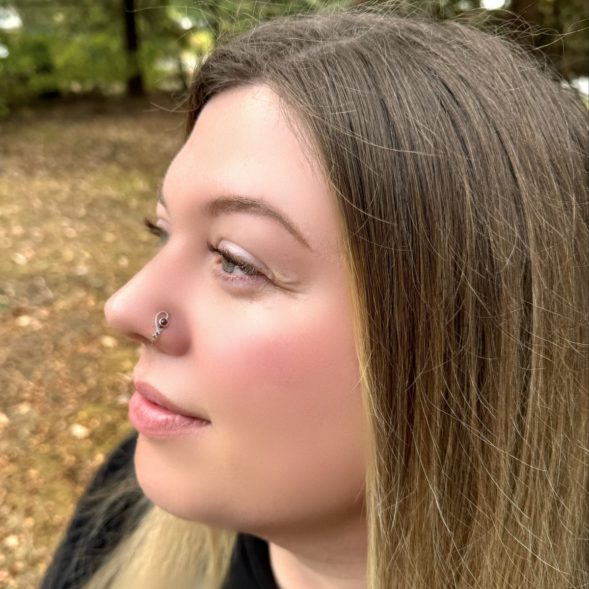 A model wearing a sterling silver hammered cuff style nose ring in an open heart design and set with a garnet gemstone.