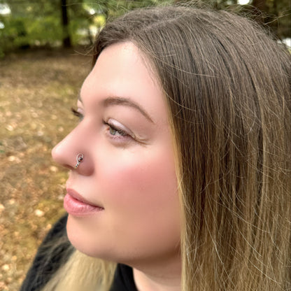 A model wearing a sterling silver hammered cuff style nose ring in an open heart design and set with a garnet gemstone.