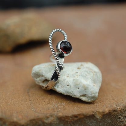 A side view of an open heart design sterling silver nose cuff set wtih a red garnet gemstone.