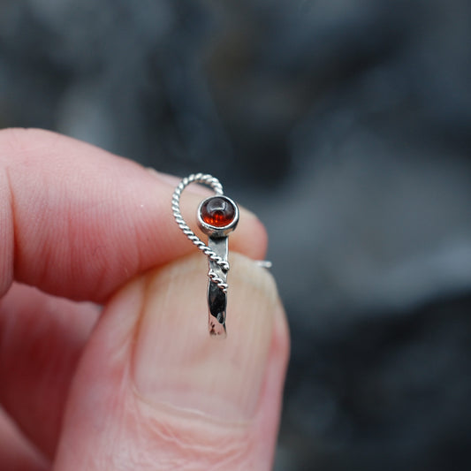 An open heart design is wrapped around a garnet gemstone on a hammered cuff sterling silver nose ring.