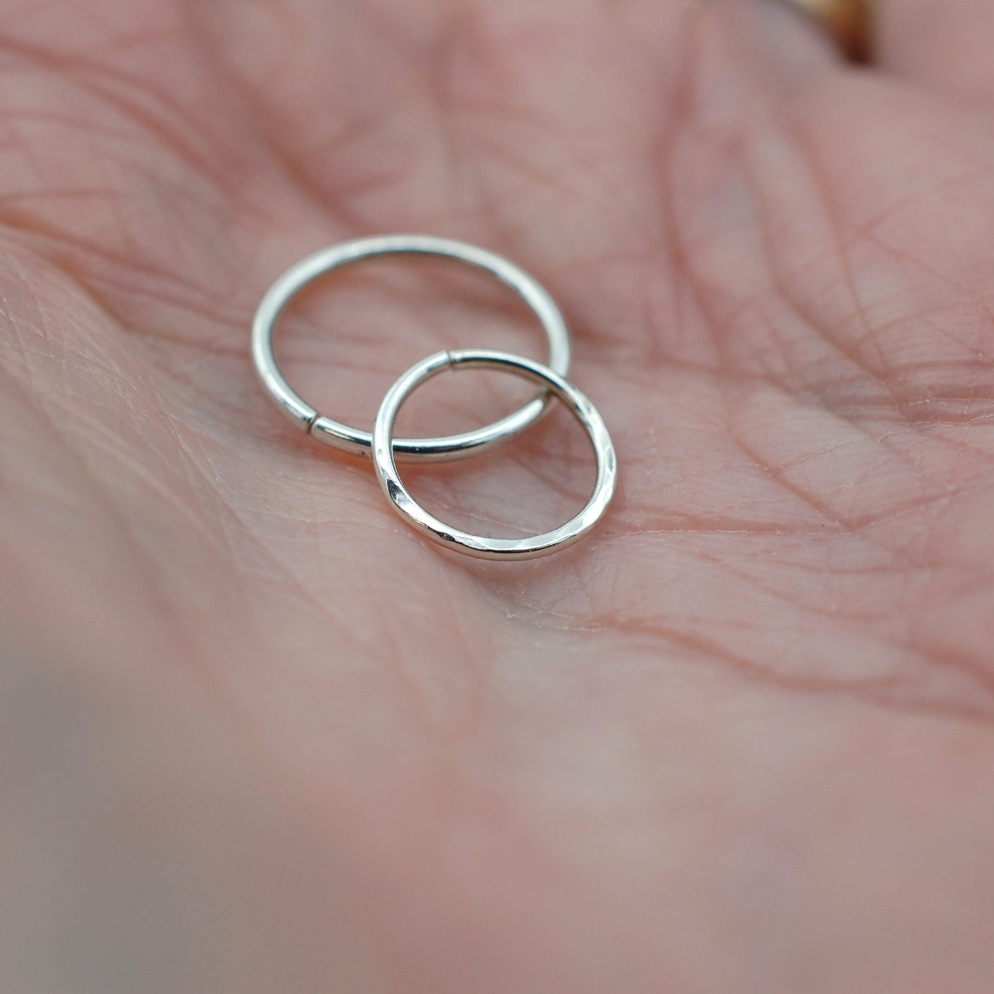 two silver nose rings held in a hand
