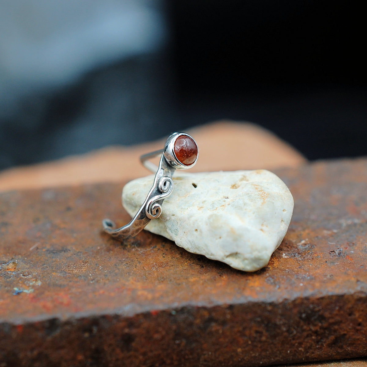 A view of a hammered sterling silver nose cuff laying across a small rock to show size.
