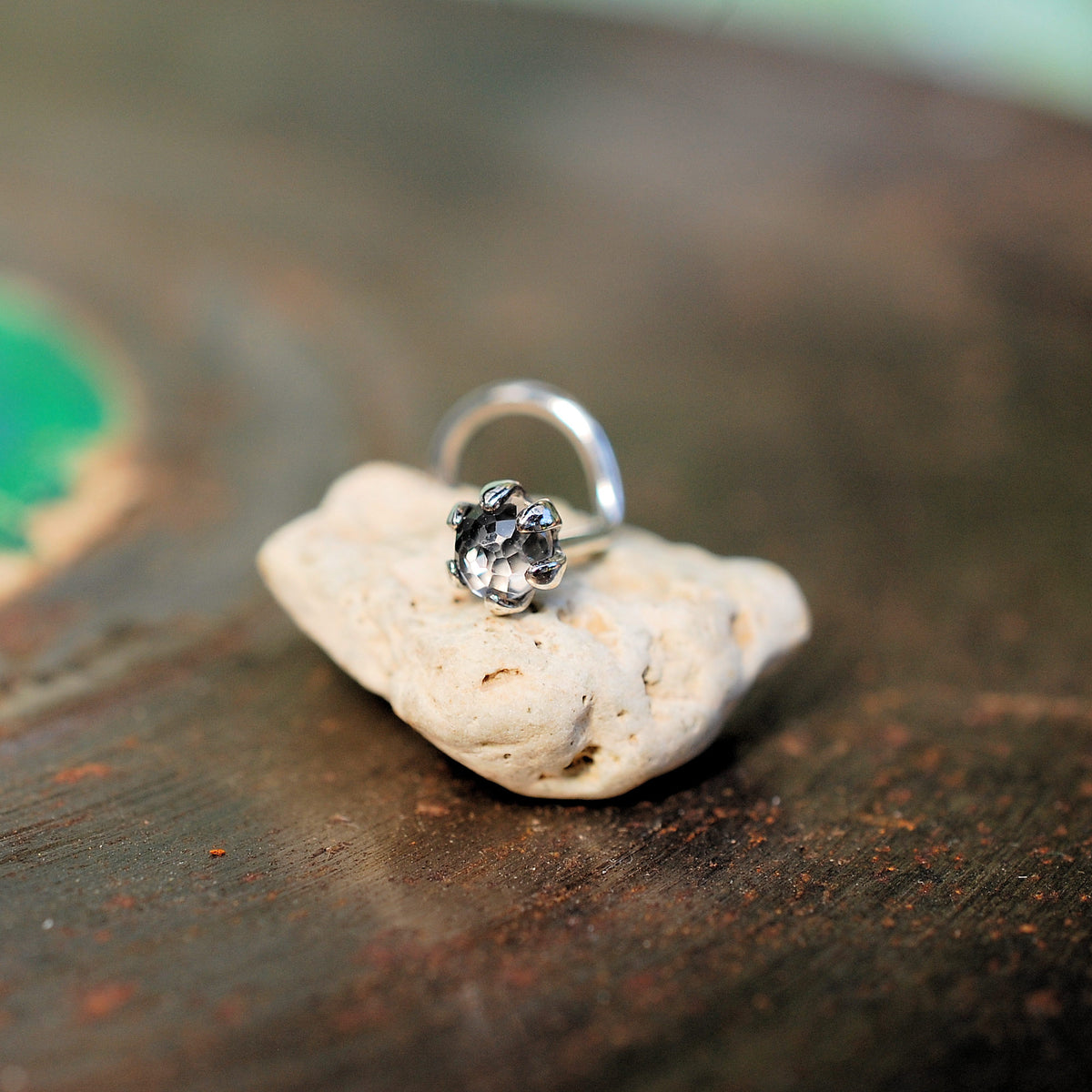 silver nose stud with white topaz sitting on a small rock