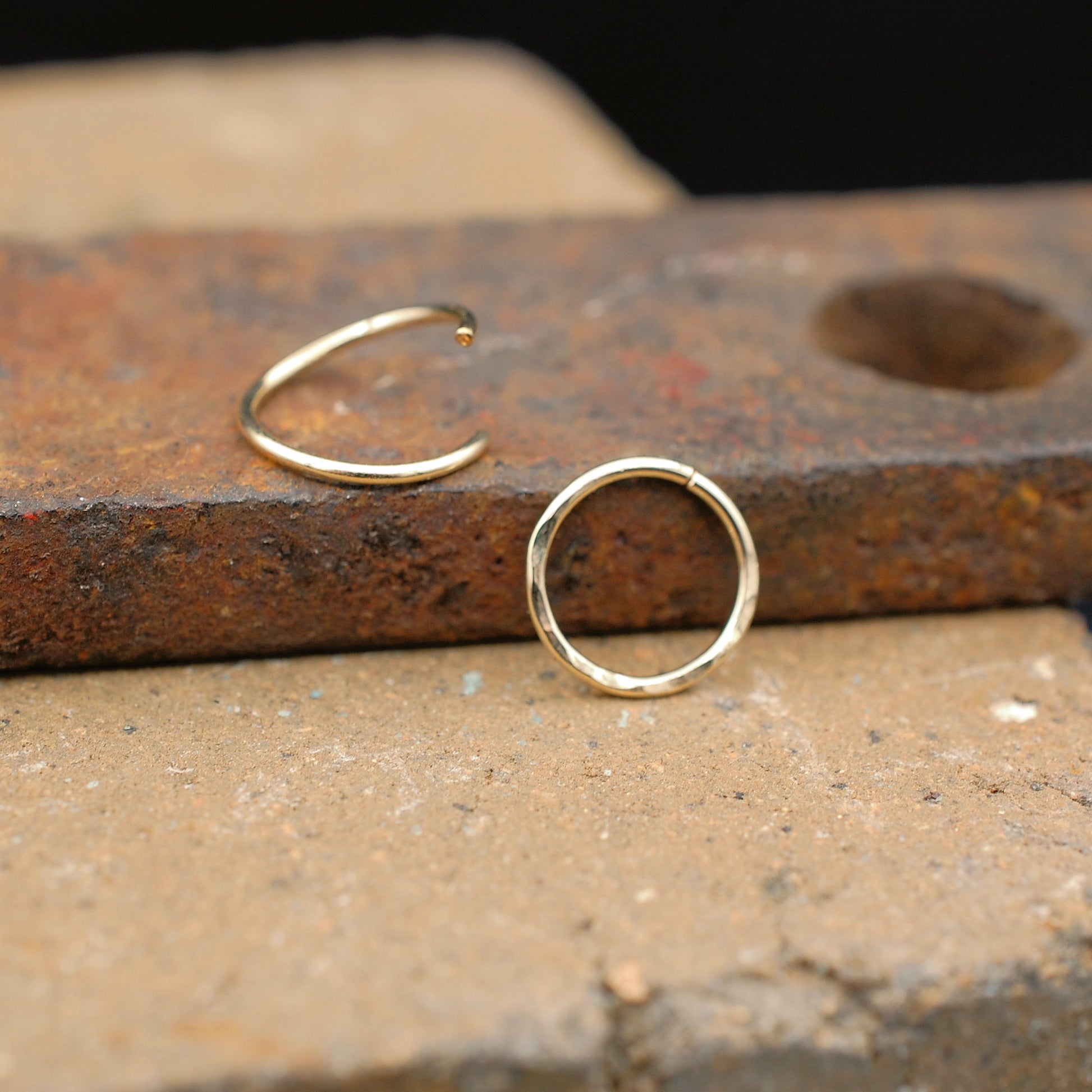 two gold nose rings displayed on a brick - hammered texture and sleek
