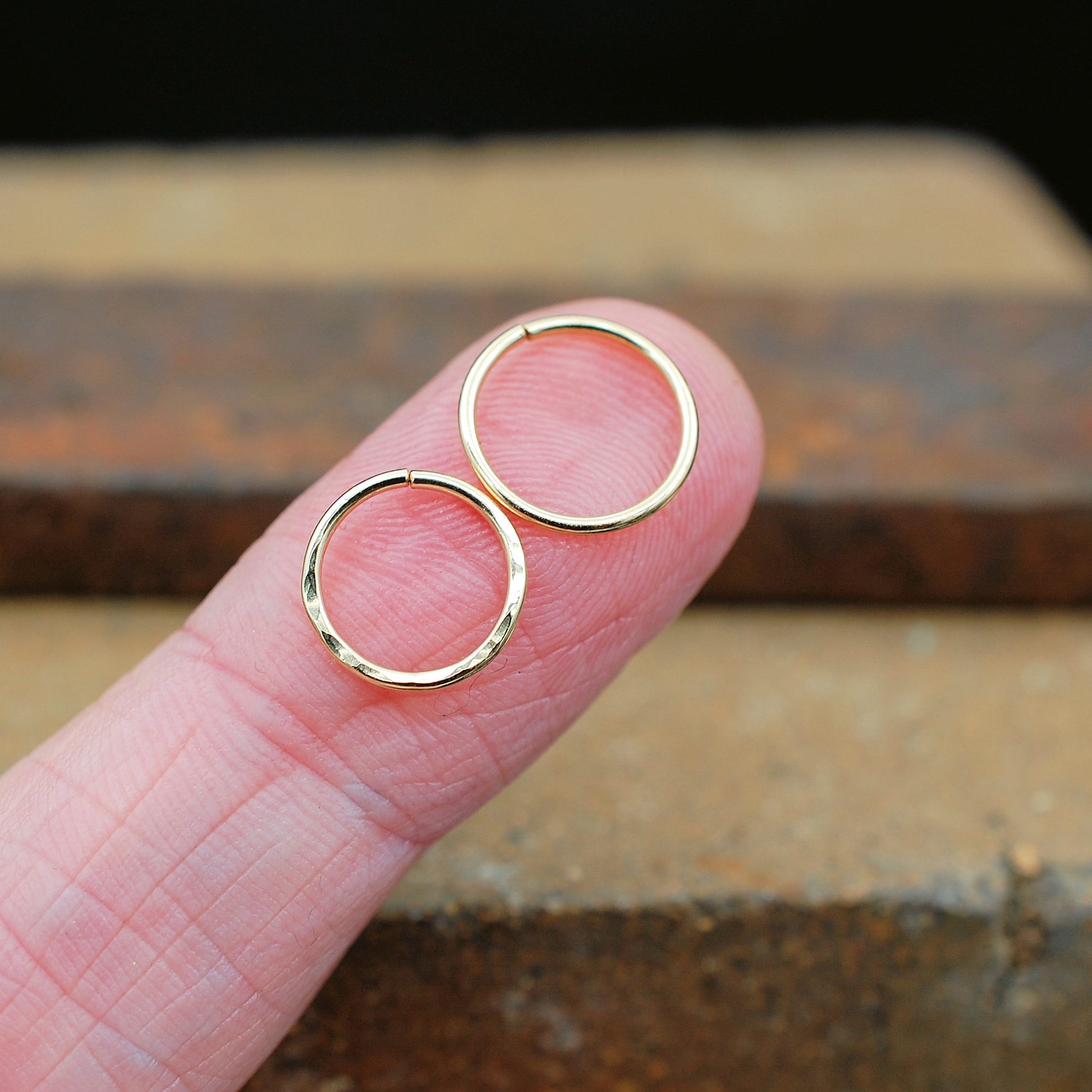 Two gold nose rings on a finger showing one sleek version and one hammered version