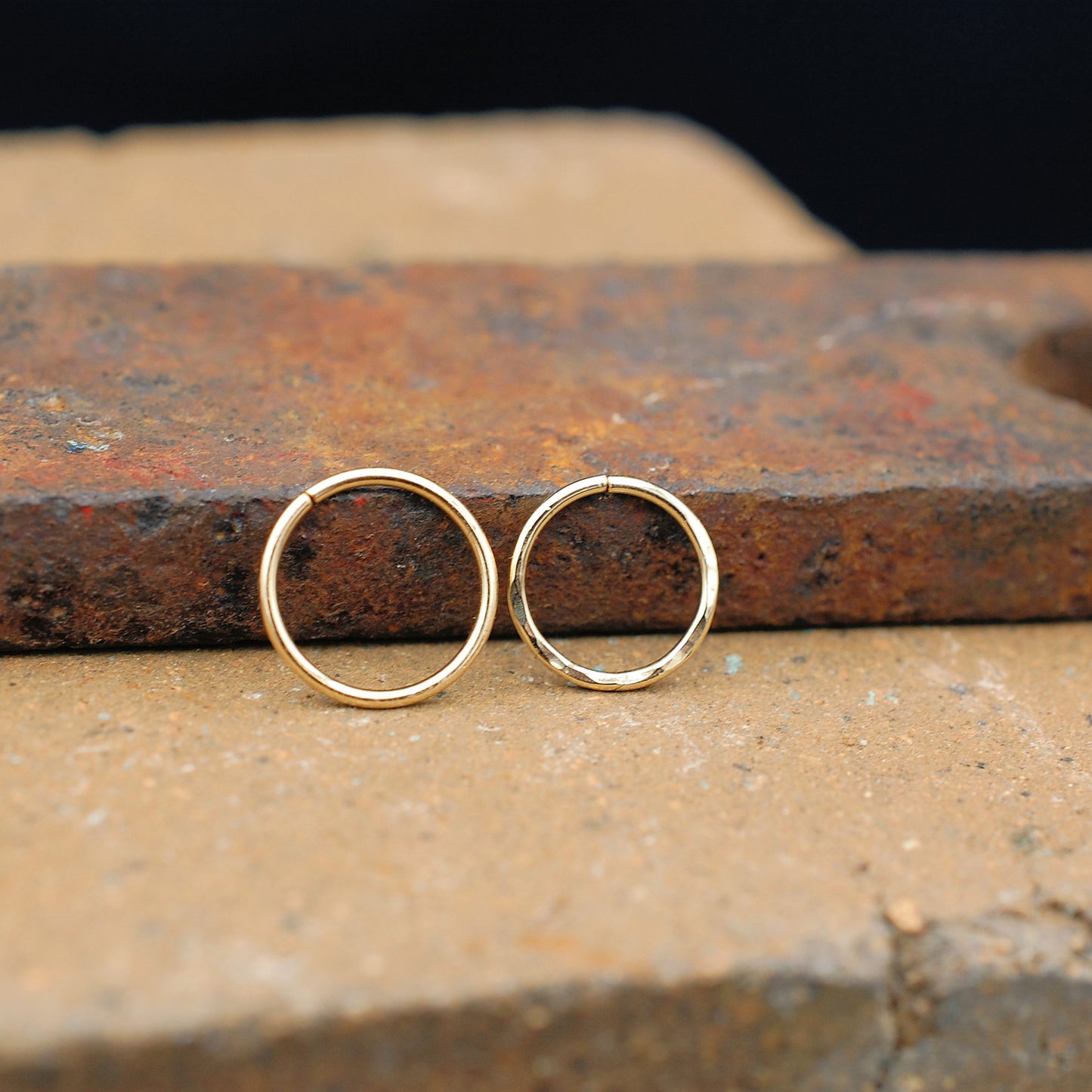 One sleek gold nose ring & one hammered gold nose ring shown on brick