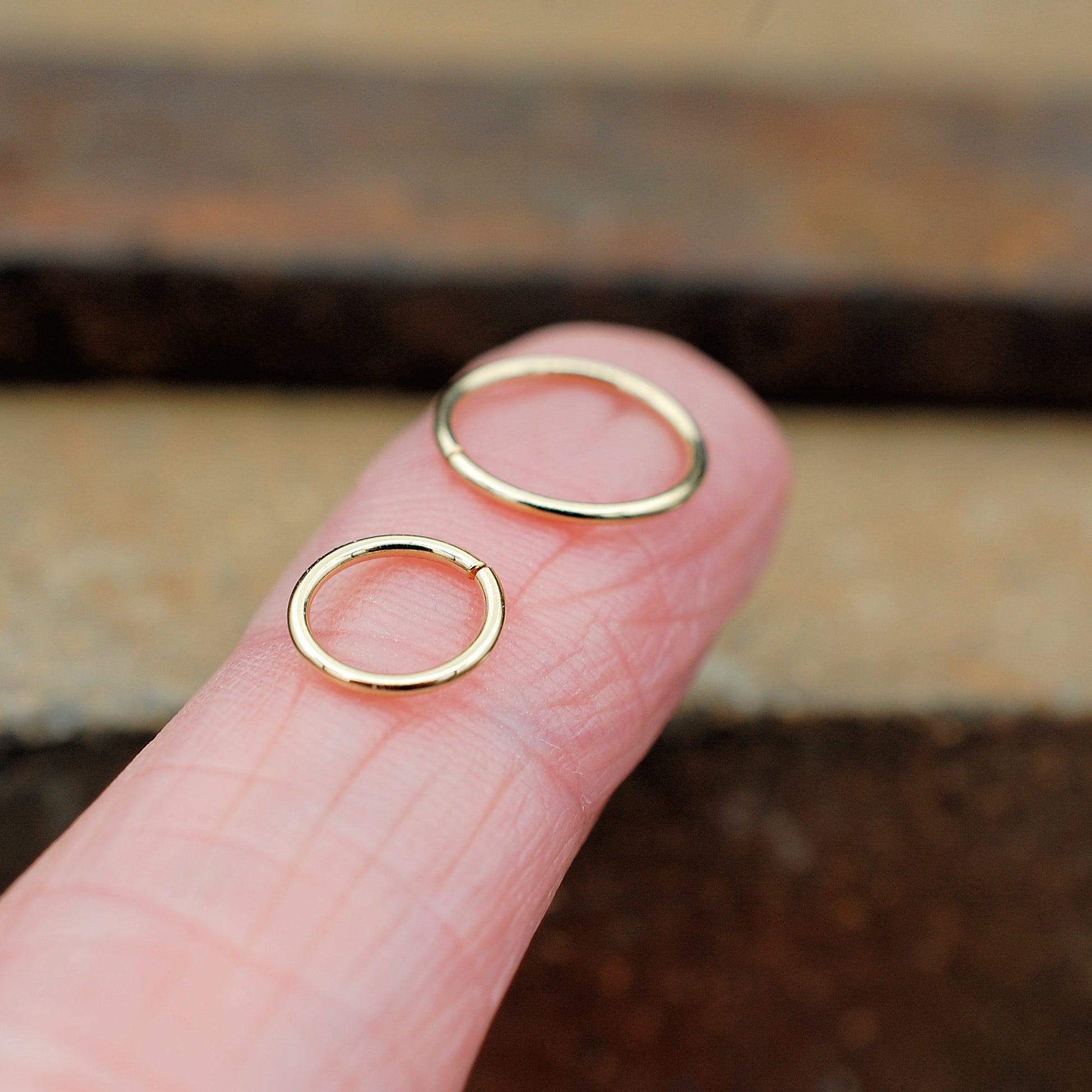 two gold nose rings on a finger for size comparison