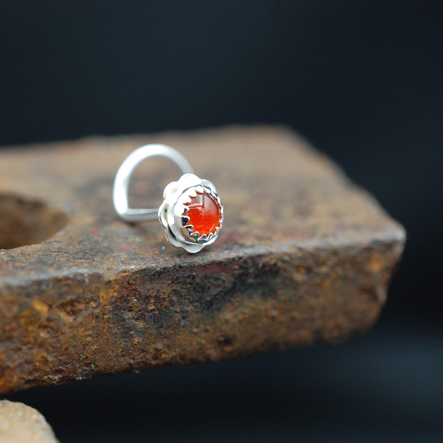 Silver nose stud with orange gemstone on a brick surface