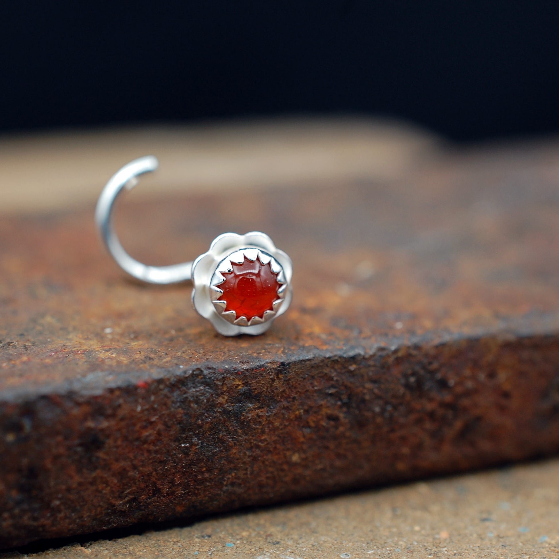 Silver nose stud with an  orange stone on a textured surface