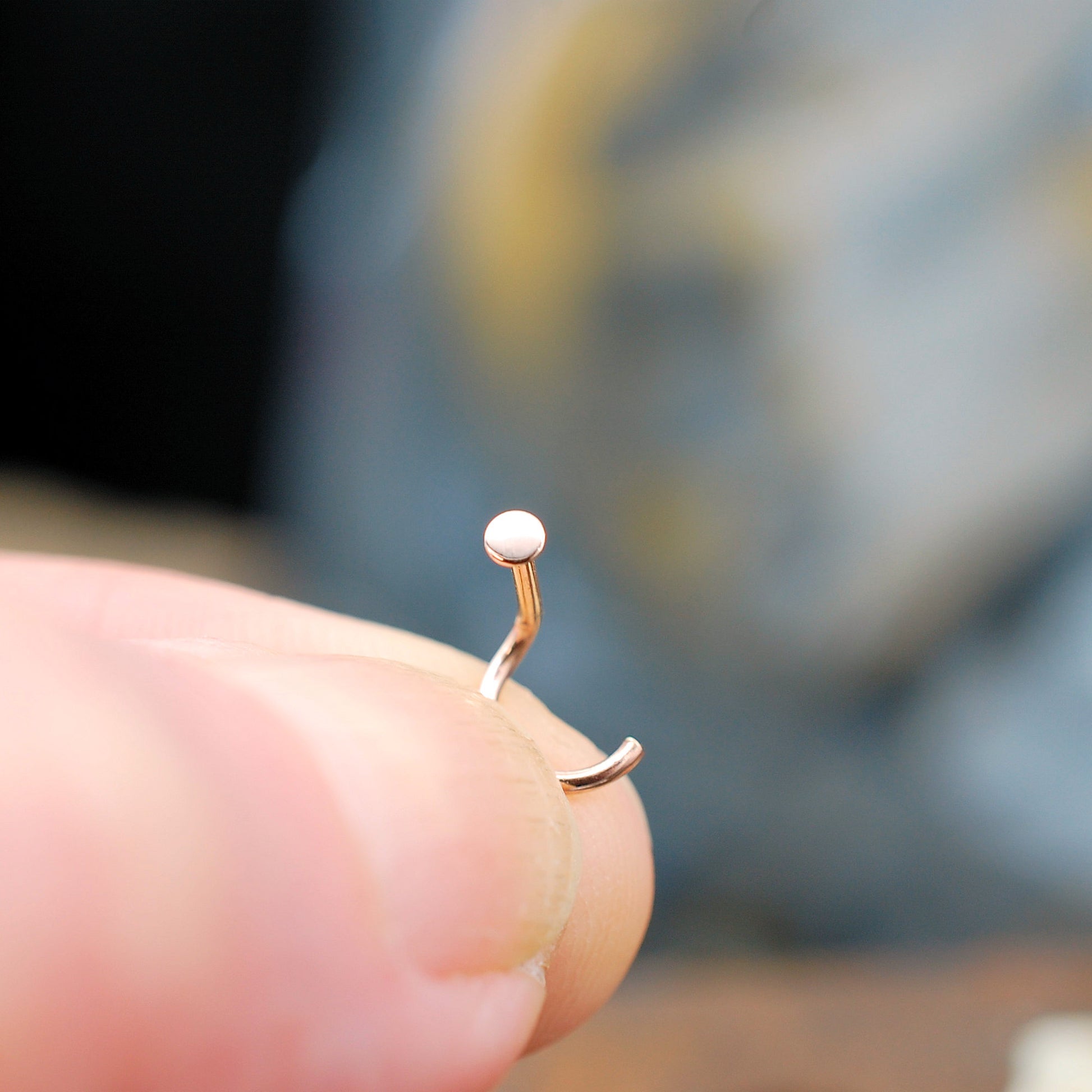 Rose gold nose ring on a finger with a blurred background