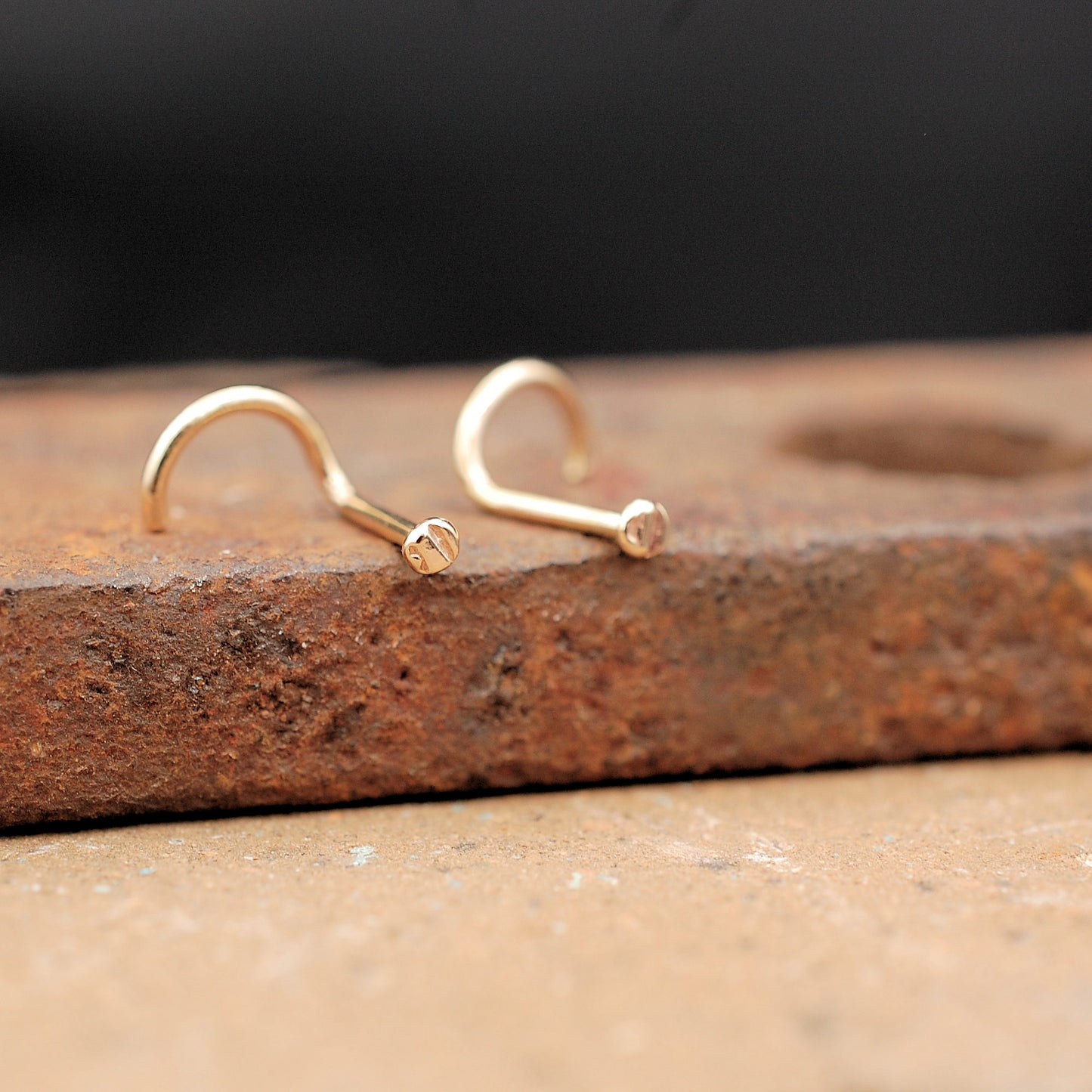 two gold nose studs on a brick