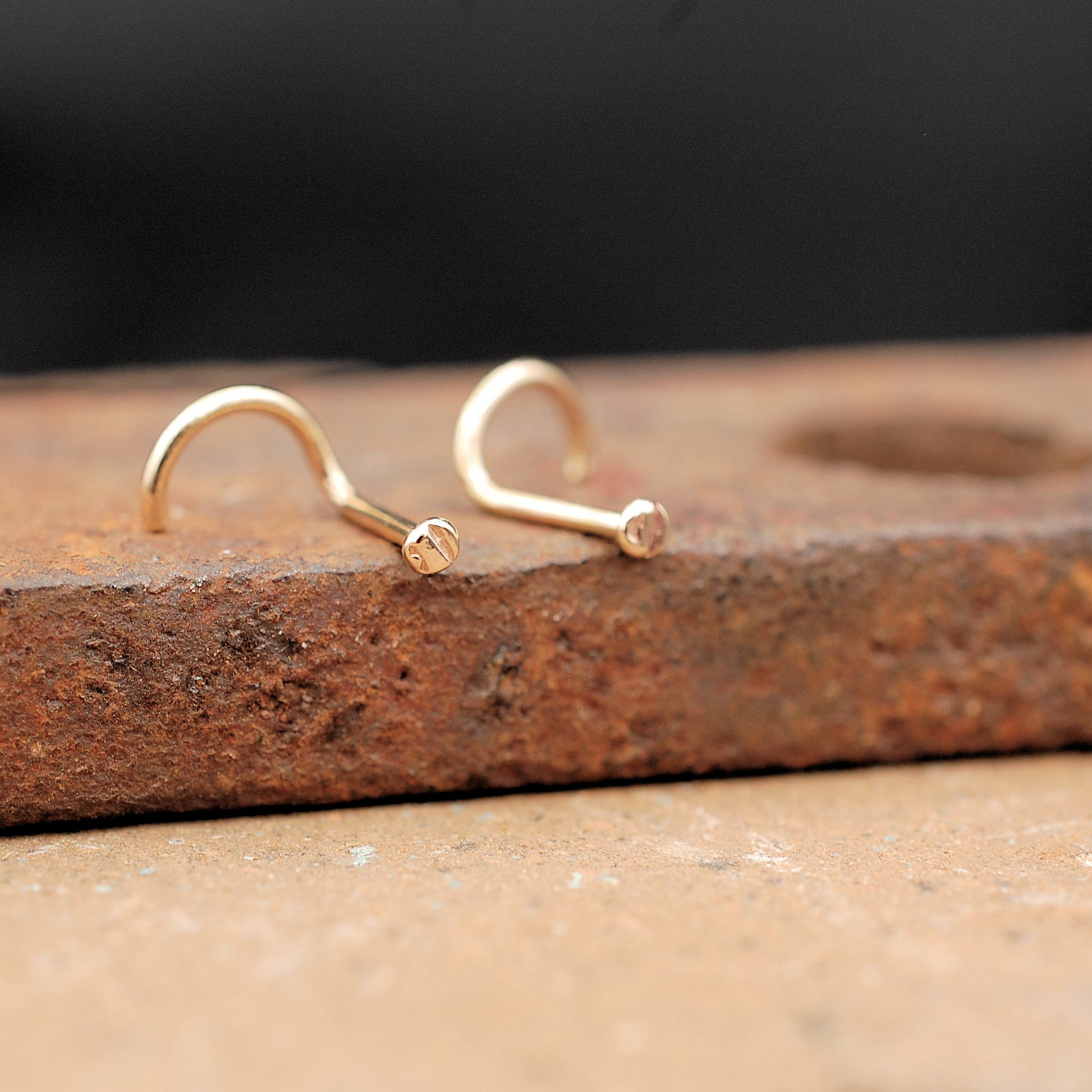 two gold nose studs on a brick