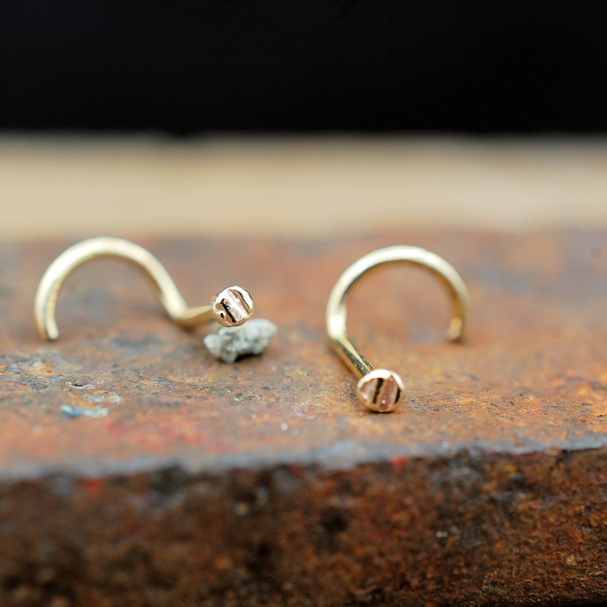 Pair gold nose studs on a brick surface