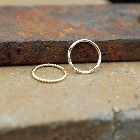 Two gold nose rings on a textured surface