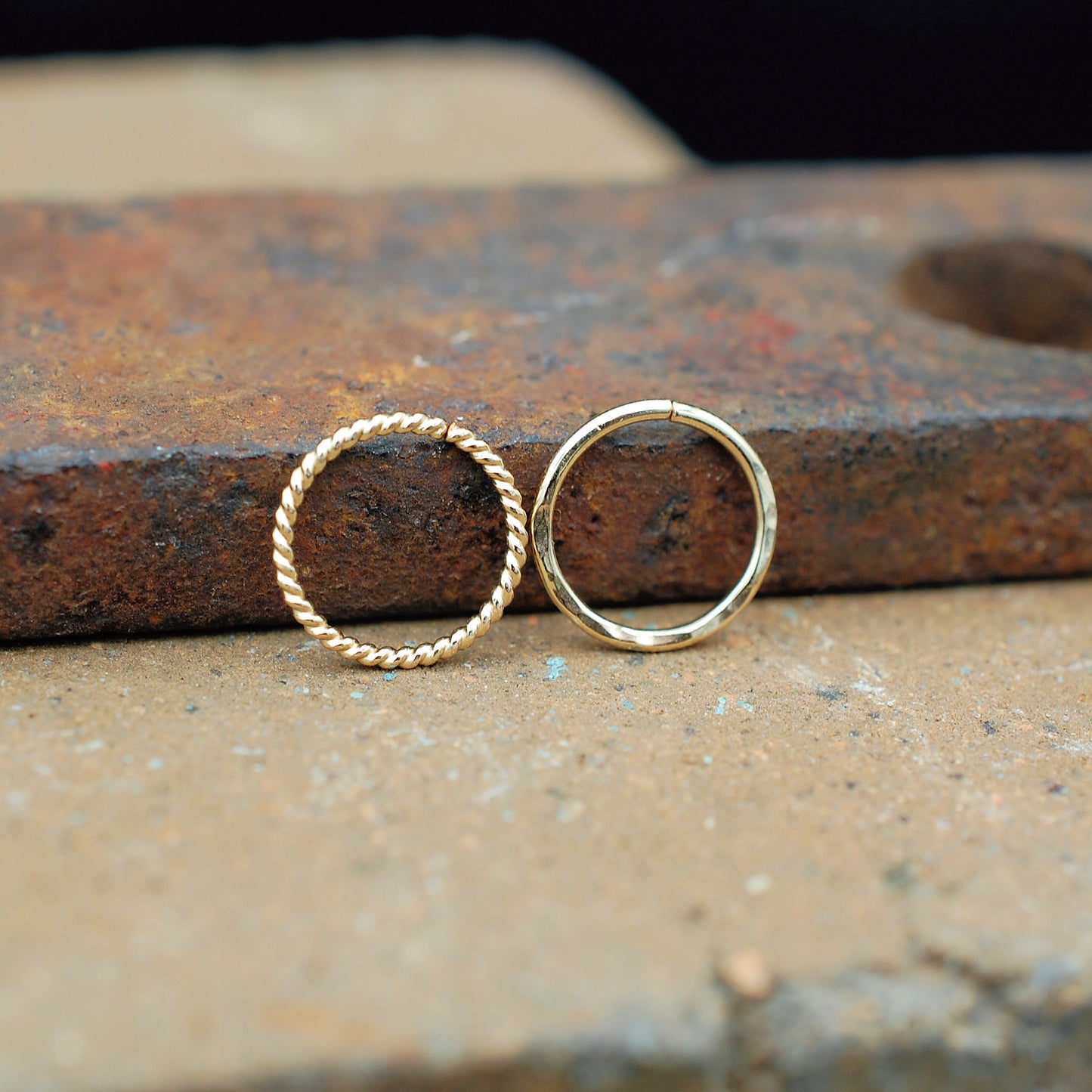 Gold hoop nose rings on a rustic metal surface