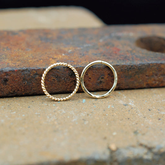 Gold hoop nose rings on a rustic metal surface