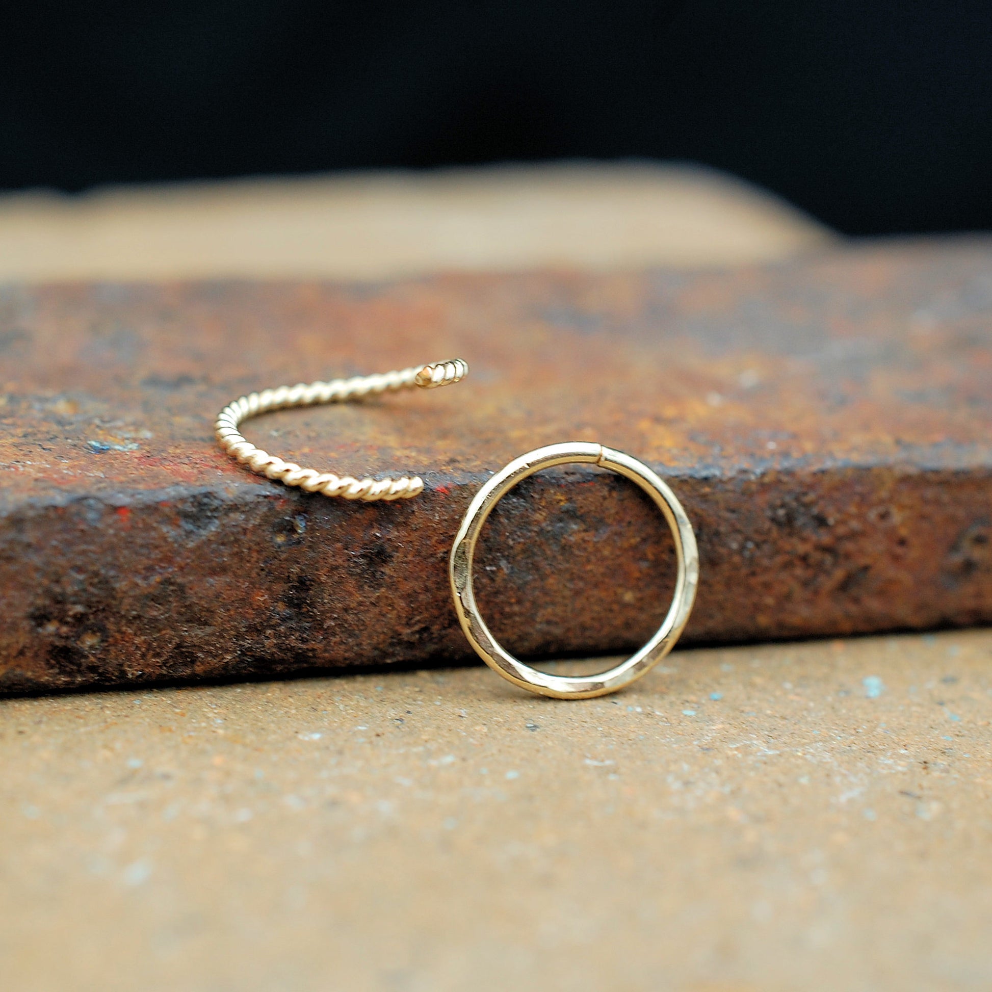 Gold twisted nose ring and gold hammered nose ring on a brick
