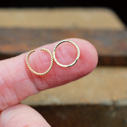 Gold hoop nose rings held between fingers against a blurred background