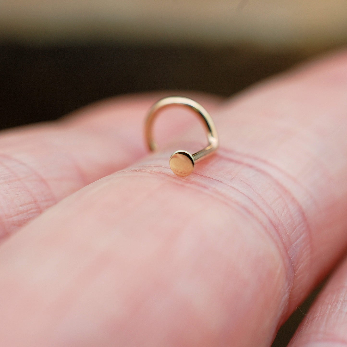 tiny gold dot nose stud on a finger