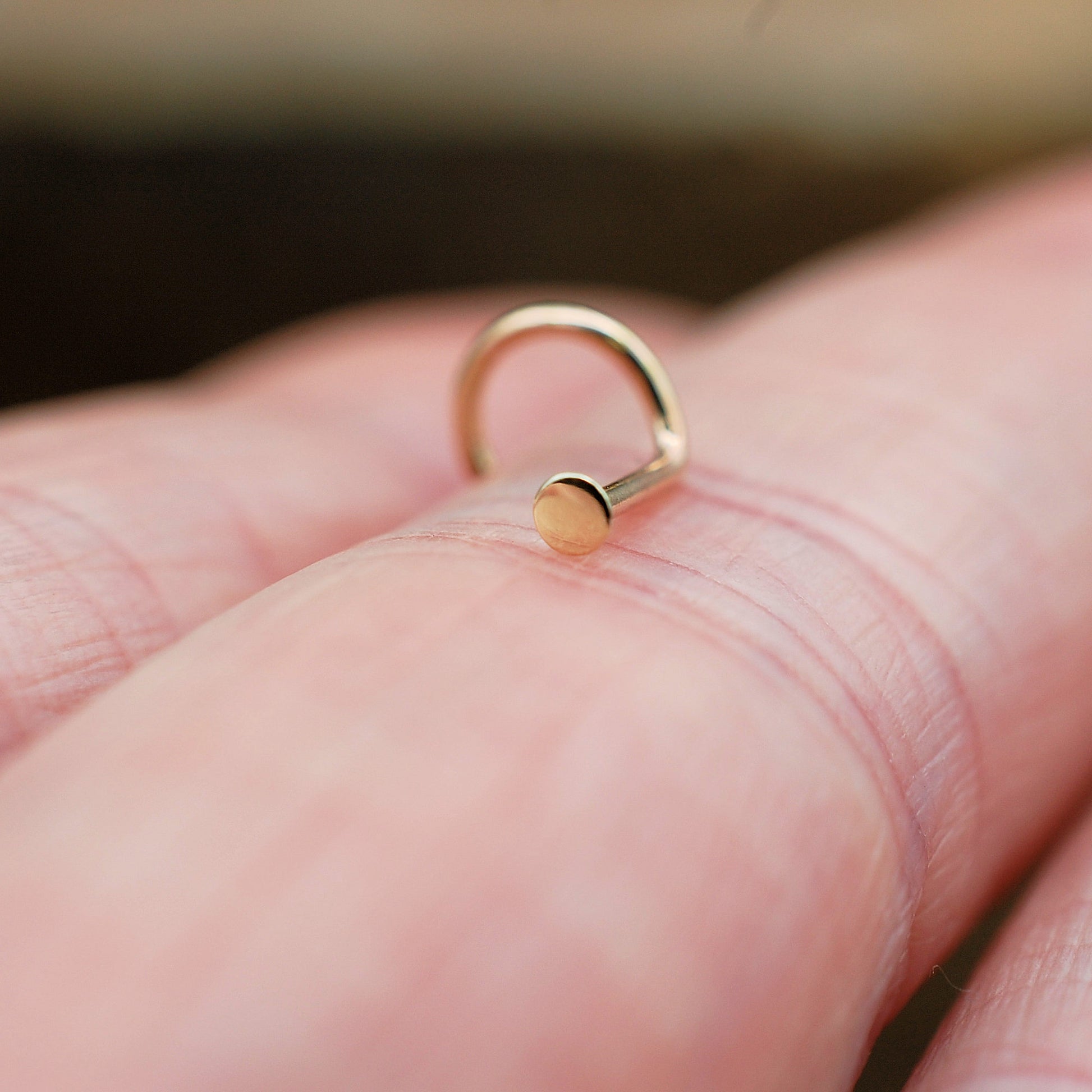 tiny gold dot nose stud on a finger